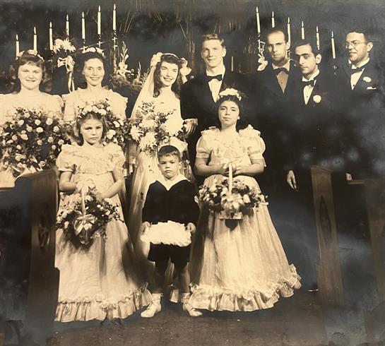 Bridal party poses for a formal portrait in wedding dresses with floral arrangements.
