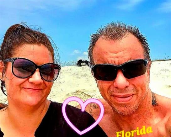 Joyful couple poses together on a sandy beach under a bright blue sky in Florida.