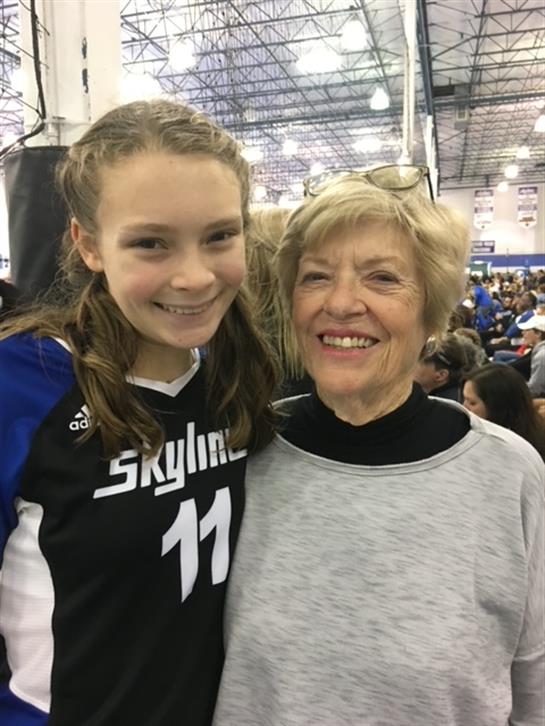 A young volleyball player smiles brightly beside her grandmother during a lively sports tournament.