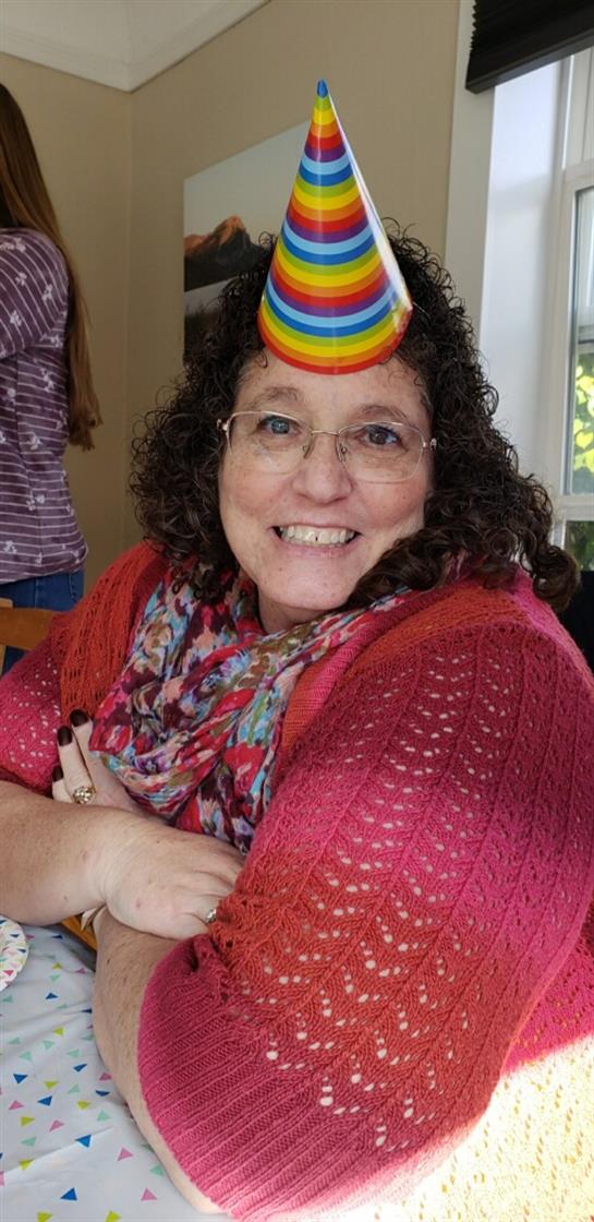 A smiling woman wearing a rainbow headband enjoys a cheerful moment at a vibrant social event.