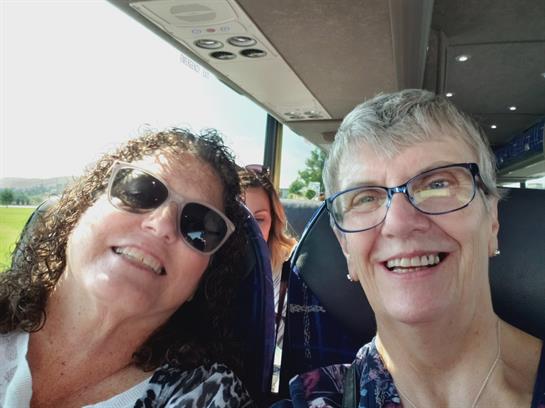 Two women with sunglasses smile together on a bus, capturing a joyful moment during their journey.