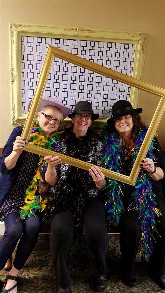 Women in hats and feather boas enjoy a playful moment in a decorated room filled with joy.