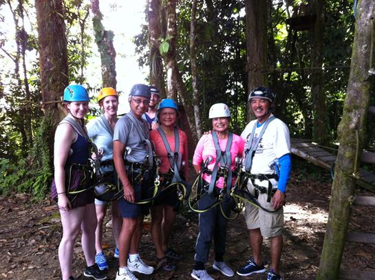 Group of thrill-seekers prepares for zip lining adventure among tall trees in vibrant forest.