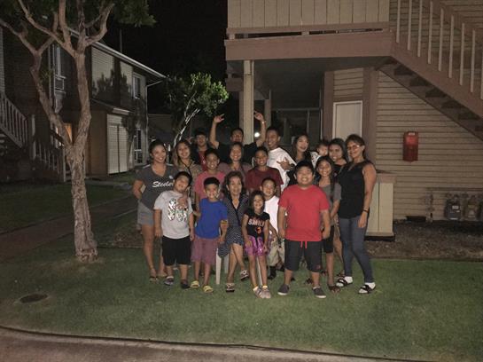 Families and children come together for a joyful gathering outside their homes at night.