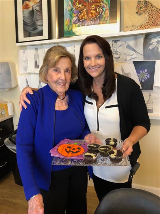 Two women share joy, showcasing colorful Halloween treats in a friendly setting.
