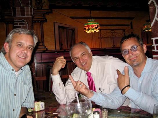 Three men are seated at a table in a restaurant, sharing laughs and engaging in conversation.