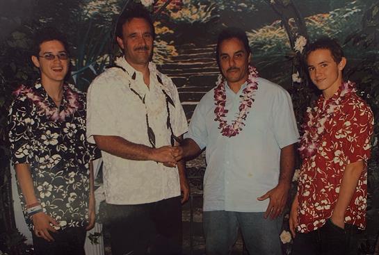Four people are celebrating in Hawaii, engaging in friendly handshakes while wearing leis.