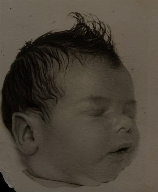 A newborn baby with spiky hair sleeping soundly against a softly lit background.