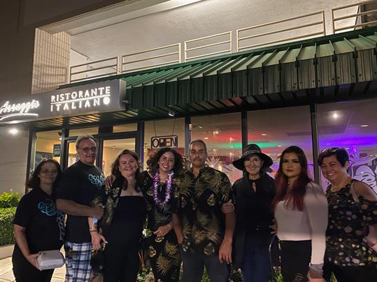 Group of friends pose happily outside an Italian restaurant at night, celebrating together.