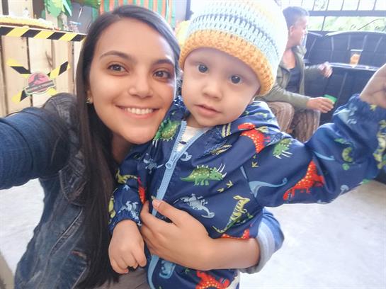 Woman poses happily with toddler wearing vibrant clothing during a cheerful event.