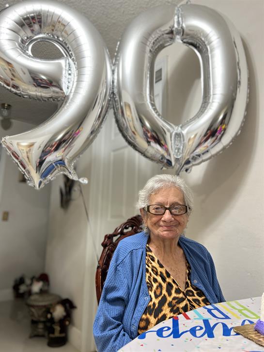 An elderly woman celebrates her 90th birthday surrounded by balloons and loved ones.