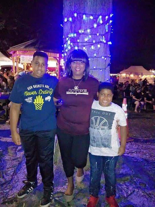 Two children smile happily alongside an adult at a fair during nighttime festivities.