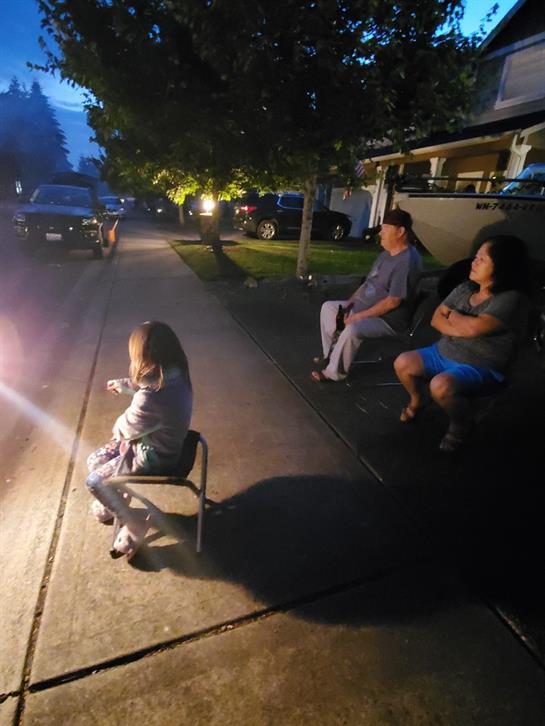 Groups gather outside their homes on a warm evening to watch colorful fireworks light up the sky.