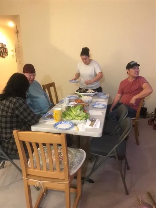 Friends dine around a table, sharing food and laughter in a warm, inviting space.