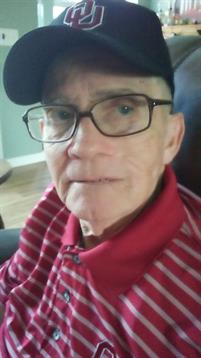 Elderly man wearing glasses and a baseball cap smiles while sitting comfortably at home.
