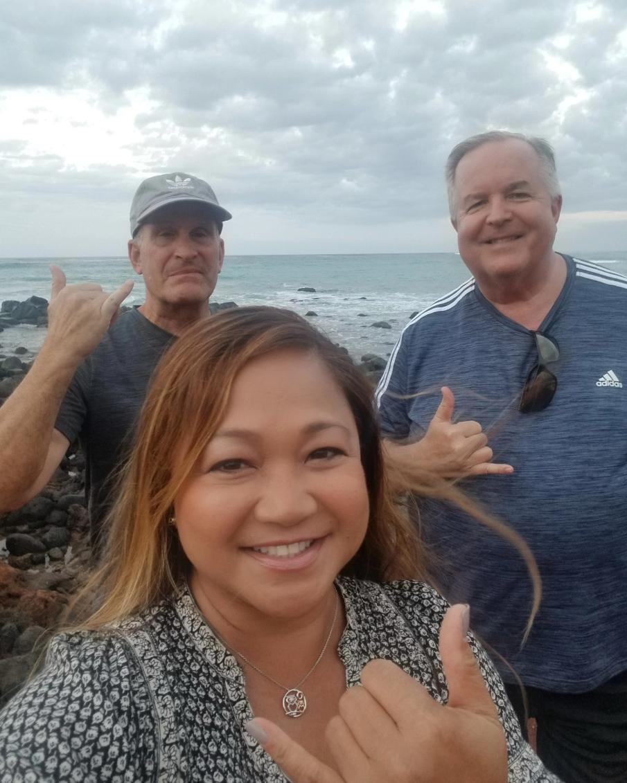 Friends make cheerful gestures near the ocean, enjoying each other's company at sunset.