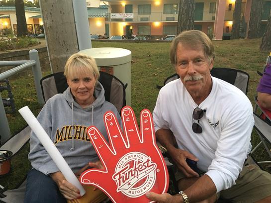 Two friends relax in chairs at a festival, holding a playful hand sign while enjoying the event.