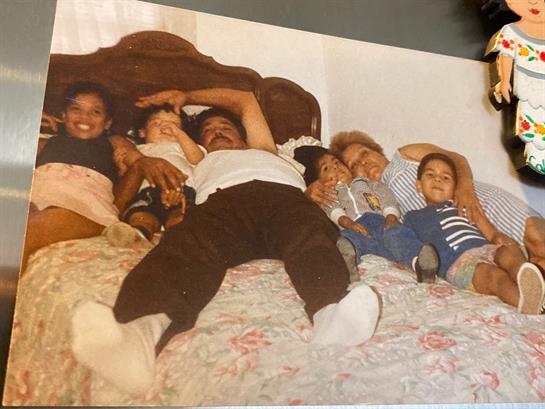Adults and kids share laughter, relaxing on a bed in a cozy room.