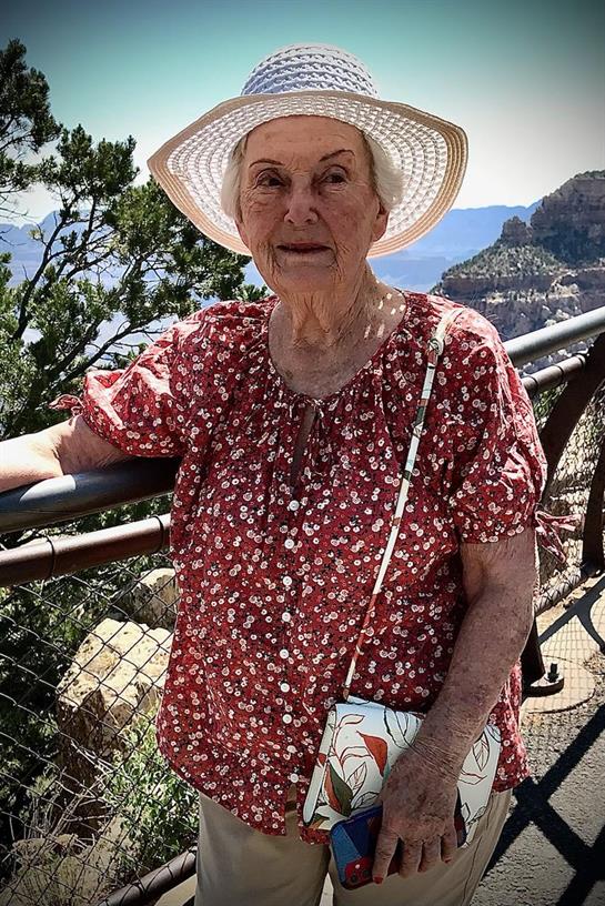 An elderly woman stands by the railing at the Grand Canyon, appreciating the vast landscape.