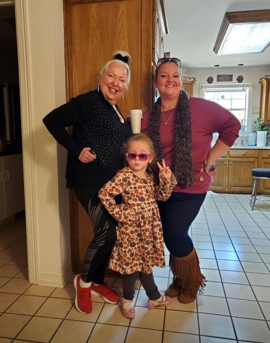 Women and girl strike fun poses in a cozy kitchen, enjoying a joyful moment together.