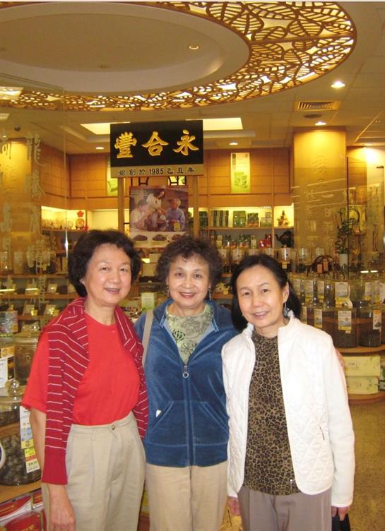 Three women smile in a busy herbal shop, exploring products and decor.