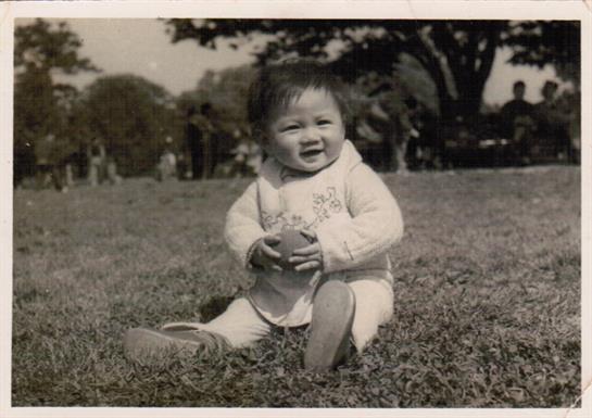 A cheerful baby sits on the grass with a ball, enjoying a sunny day in the park.
