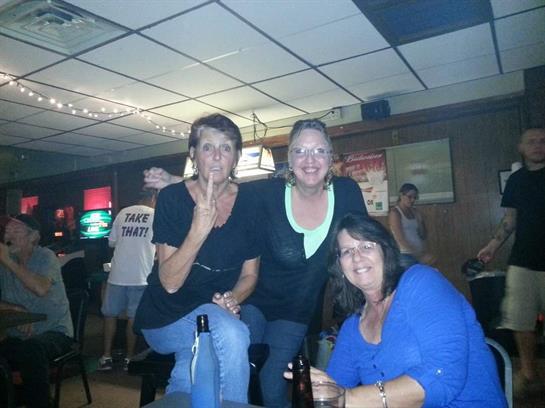 Three women pose together, laughing and having fun in a bustling local bar at night.