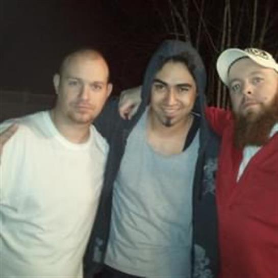 Group of three friends smiling and standing close together during a nighttime gathering.