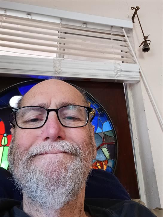 A smiling person with glasses sits by a colorful stained glass window, savoring the moment.