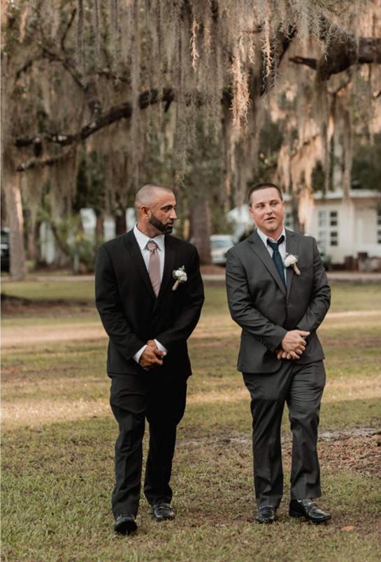 Two well-dressed men stroll through a beautiful outdoor venue as part of a wedding celebration.