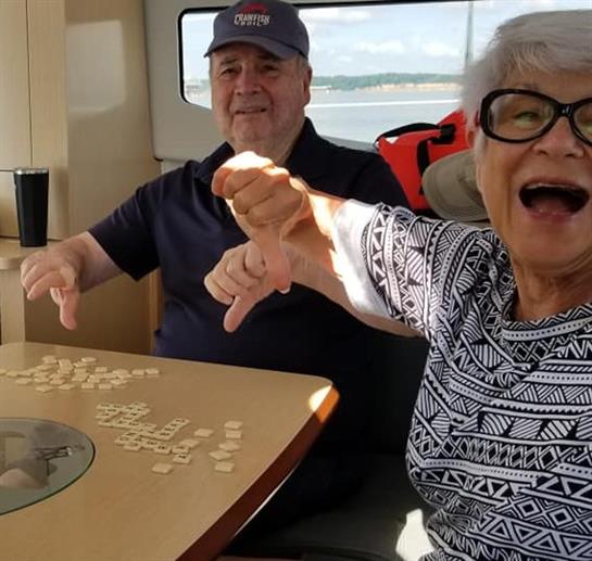 Two seniors are joyfully playing dominos on a boat, surrounded by water under clear skies.