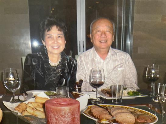 Couple smiles while dining with friends, surrounded by food and drinks in a warm atmosphere.