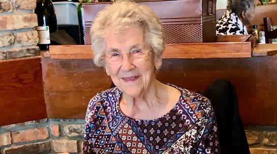 An elderly woman with silver hair enjoys a cheerful moment at a cafe, radiating warmth and joy.