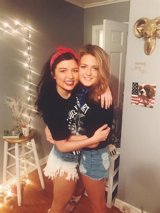 Two women smile and hug in a warmly lit room, showcasing friendship and joy in a relaxed setting.