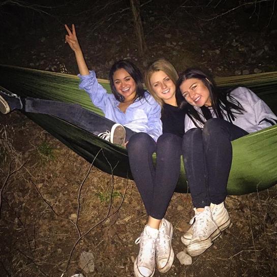 Three friends relax together in a hammock, sharing laughter and joy during a night outdoors.