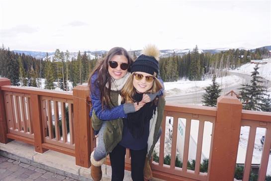 Two friends smile and enjoy the snowy mountains in their winter outfits.