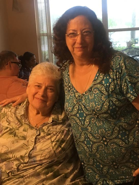 Two women share a warm moment together at a family gathering, surrounded by loved ones.