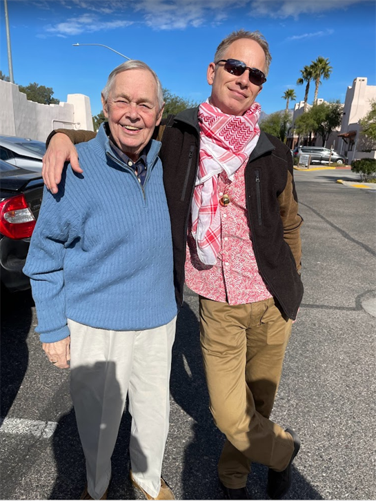 Two men are standing together in a parking lot, smiling and enjoying the sunny day.