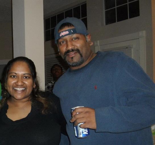 Two individuals pose happily together at a relaxed gathering in a home, showcasing smiles.