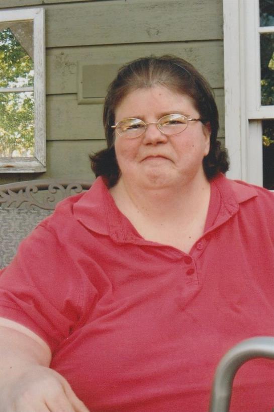 A woman in a red shirt sits comfortably on a porch, smiling and enjoying a sunny afternoon.