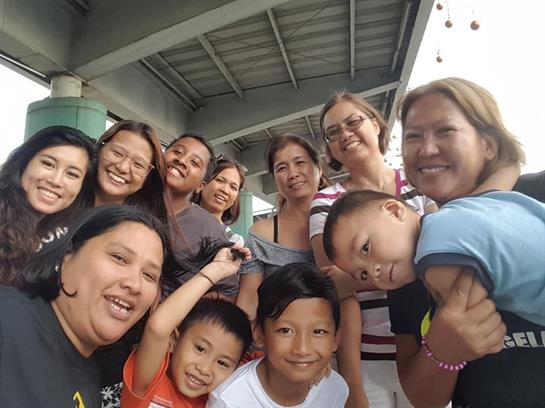 A joyful group of adults and children share smiles while posing outdoors in a lively setting.