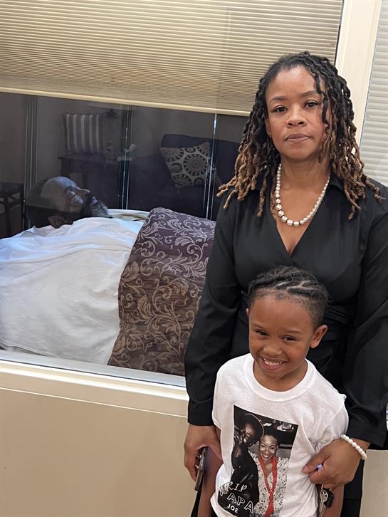 An adult woman stands beside a smiling child in a warm living space during the evening.