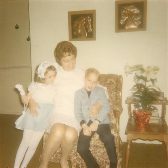 A woman sits on a chair surrounded by two young children, engaged in a cheerful moment together.