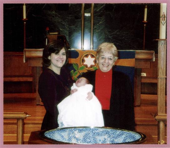 A family gathers in church to joyfully celebrate a baptism with a baby in white.