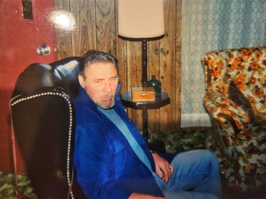 A man sits comfortably in an armchair, dressed in a blue jacket, enjoying the cozy atmosphere.