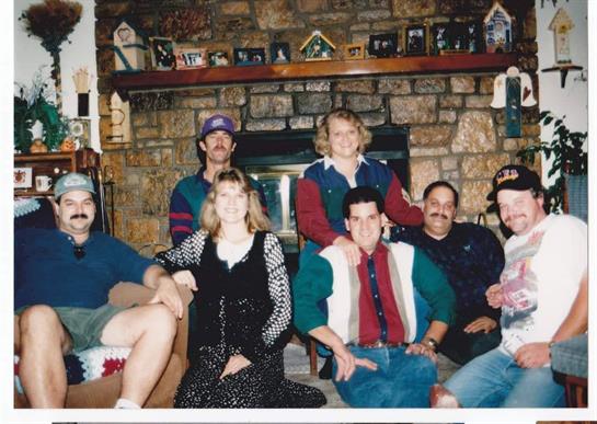 People sit together in a warm living room, posing for a joyful family photo near a fireplace.