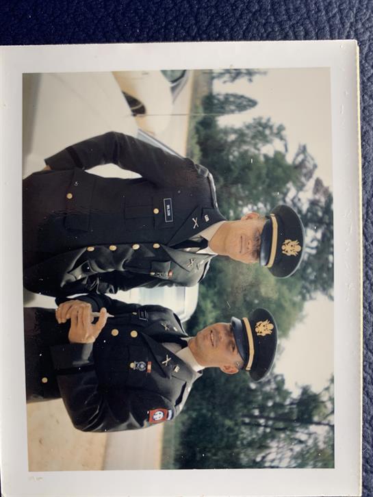 Two officers in military uniforms stand together outside, engaging with each other in conversation.