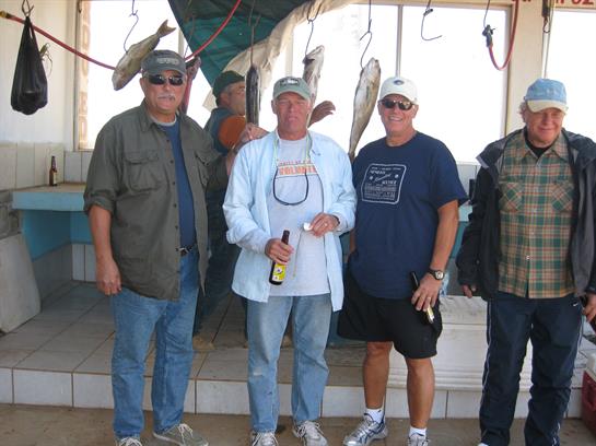 Five fishermen gather together with their catch, smiling and chatting after a successful outing.