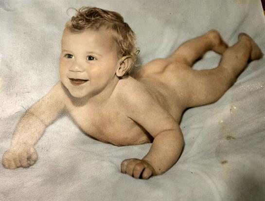 A cheerful baby with curls enjoys tummy time on a soft surface, displaying a joyful expression.