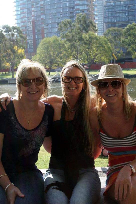Three friends relax by a river on a sunny day, enjoying each other's company and the outdoors.